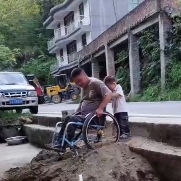  Cậu con trai&nbsp;gần 3 tuổi quá nhỏ bé bên bố và chiếc xe lăn.&nbsp;(Ảnh: Chụp màn hình Douyin)&nbsp;