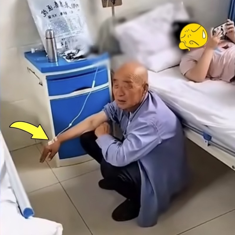  Người ông tay vẫn đang truyền phải ngồi dưới đất, nhường giường cho cháu nằm chơi điện thoại. (Ảnh: Chụp màn hình Sina)