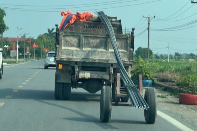 Ô tô kéo xe tự chế chở sắt thép dài hàng chục mét trên đường. Ảnh: Báo Dân trí.
