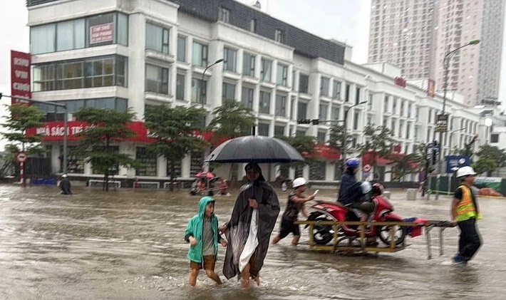 Hà Nội ảnh hưởng bão Bualoi, nhiều tuyến phố ngập sâu, không thể di chuyển bằng ô tô, xe máy nên dù trời mưa lớn phụ huynh vẫn phải đi bộ đến đón con. (Ảnh: Tuổi trẻ)