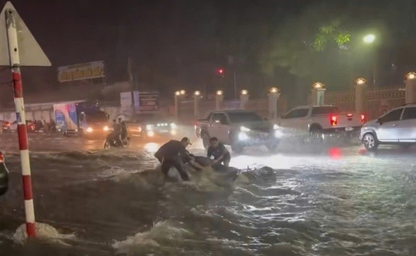 Người đàn ông cùng xe máy bị trôi giữa dòng nước, và được 3 thanh niên ra hỗ trợ. (Ảnh: Thanh niên)