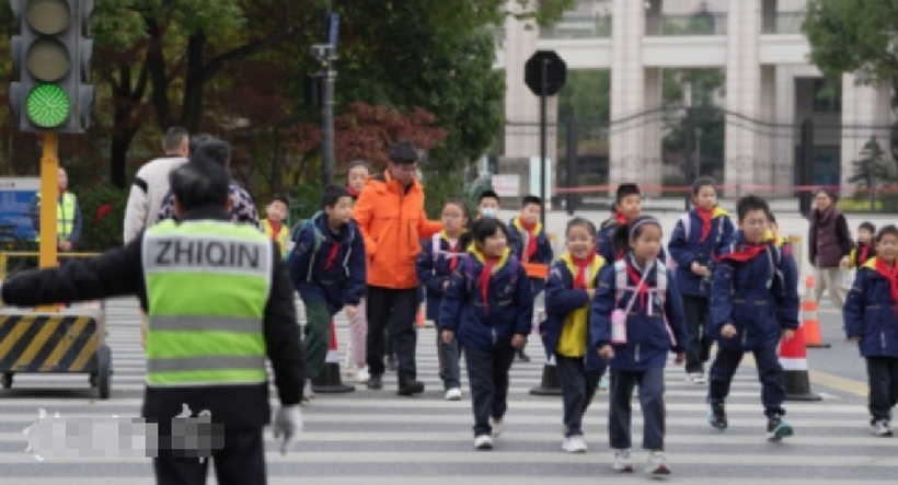 Ông quan sát kỹ các làn xe, dứt khoát ra hiệu cho tài xế dừng lại rồi nhanh chóng thúc giục học sinh qua đường. Ảnh: Hangzhou Daily.