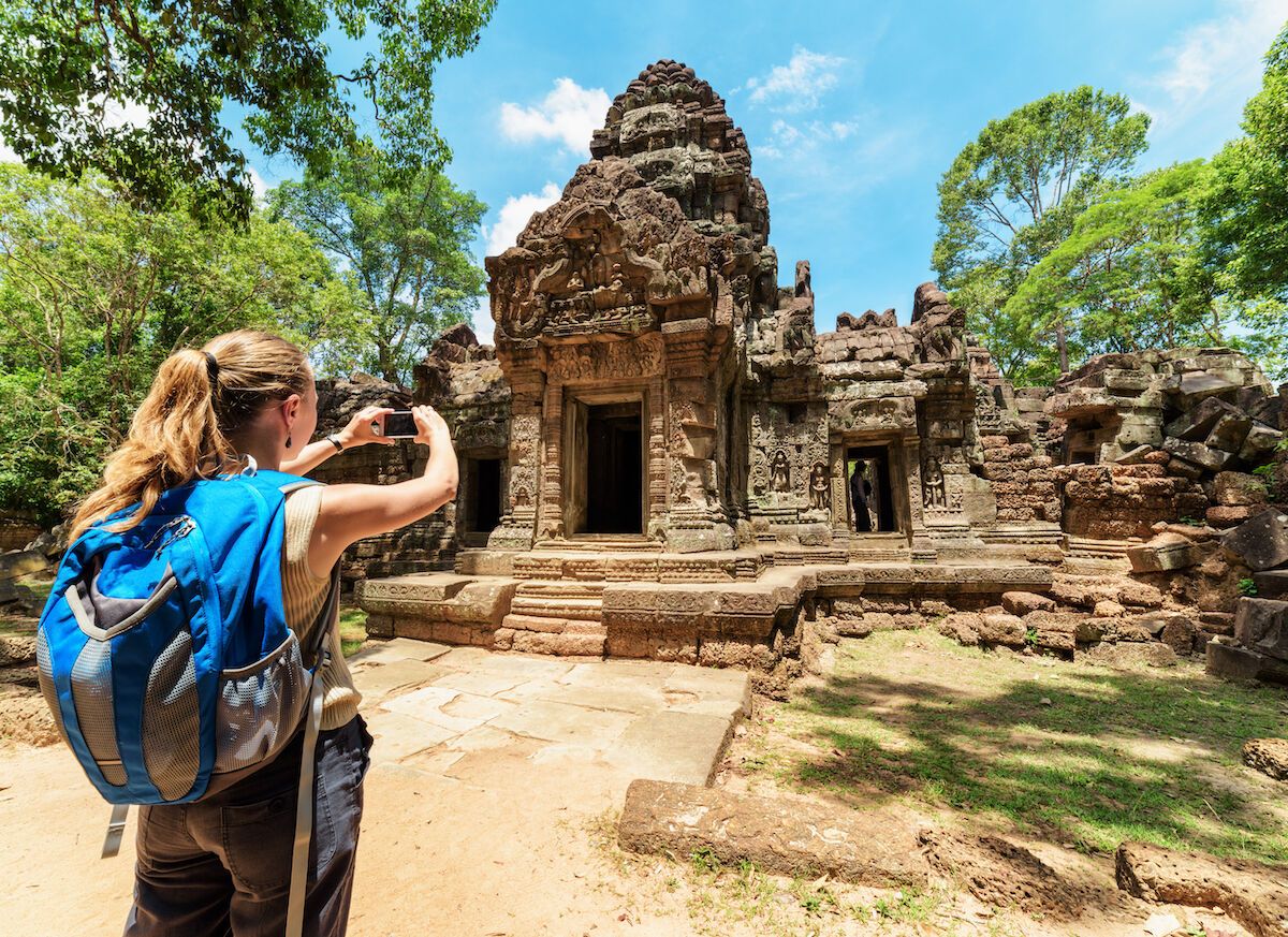 female tourist taking pictures of preah khan temple in angkor wat seam reap cambodia 1200x873