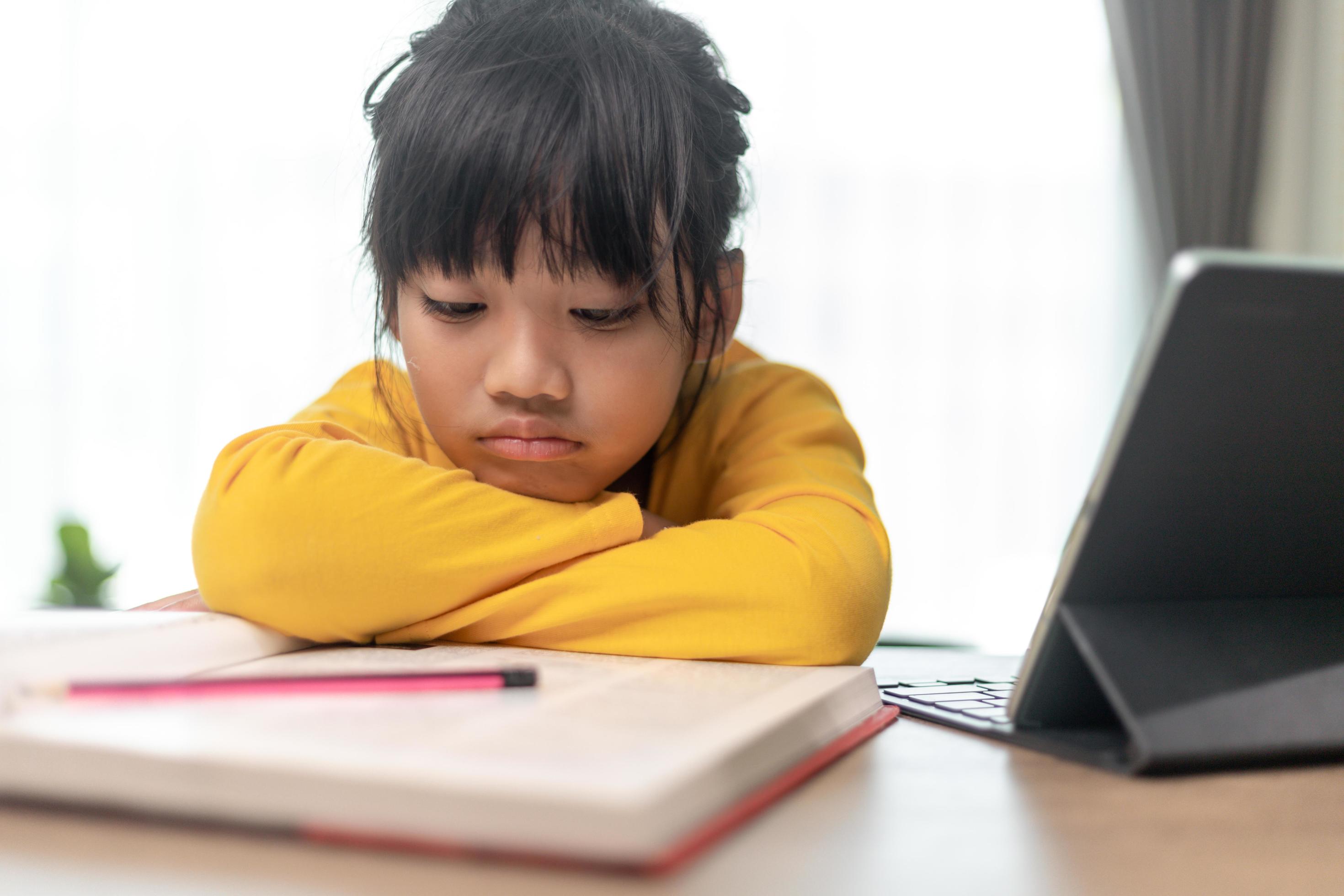little asian girl sitting alone and looking out with a bored face preschool child laying head down on the table with sad bored with homework spoiled child free photo