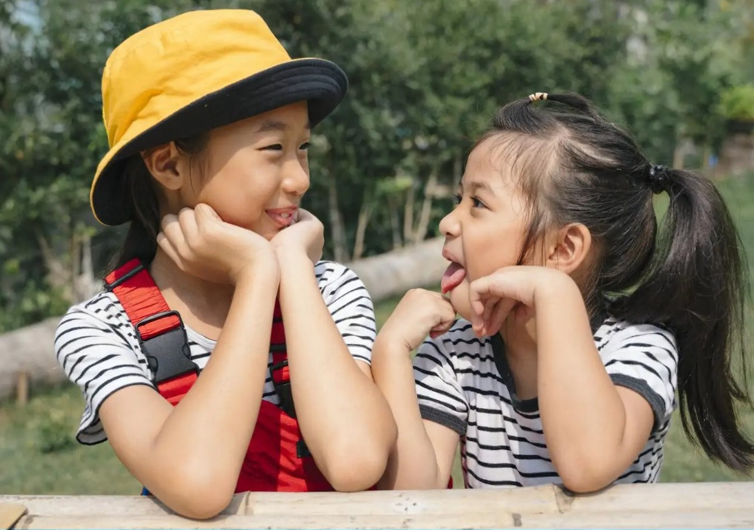 edit close up playful asian girl sitting bench little having fun each other garden park two sister green field 191380814 17765199366141155591059