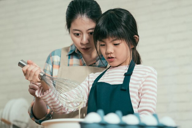 close up elegant asian chinese mom adorable young chef little girl apron mixing flour with whisk baking cooking easter cake woman teaching child daughter make bread mothers day678158 1344