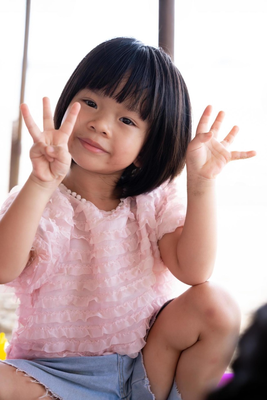 portrait of child 4 5 year old cute asian girl smiling sweetly looking at camera kid holds up four fingers on one side of three fingers to pose for vertical image photo