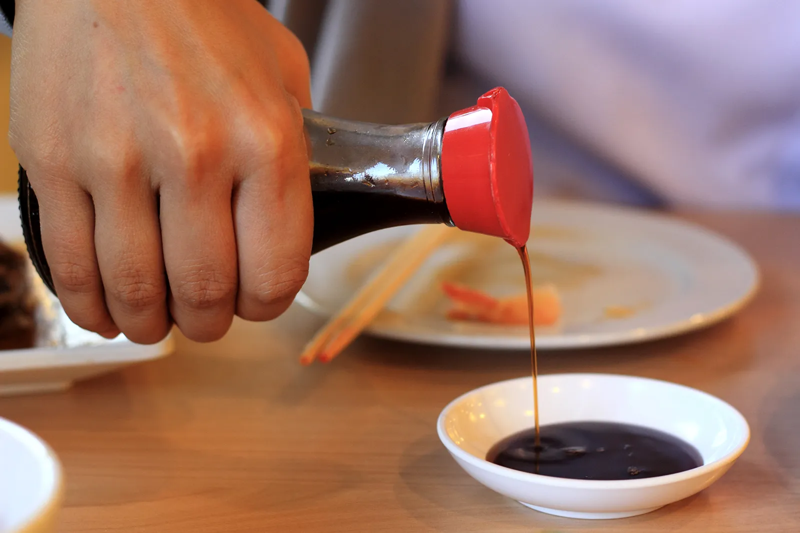pouring soy sauce from a bottle to a small dipping bowl
