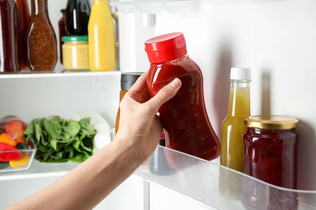 woman getting red sauce out of fridge door