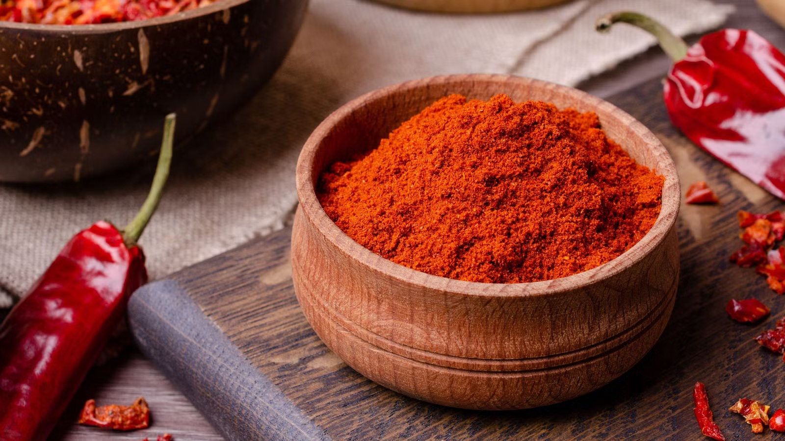cayenne pepper powder in wooden bowl surrounded by peppers